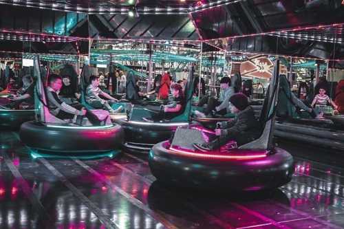 A vibrant indoor amusement area with kids enjoying bumper cars, surrounded by colorful lights and reflections.