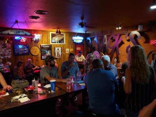 A lively bar scene with patrons chatting, neon lights, and a rustic wooden interior. Drinks are on the counter.