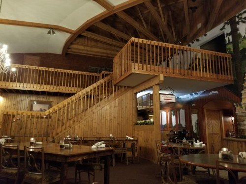 Interior of a rustic restaurant featuring wooden decor, a staircase, and tables set for dining.