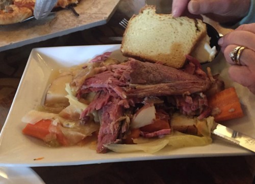 A plate of corned beef with cabbage, carrots, and potatoes, accompanied by a slice of bread.