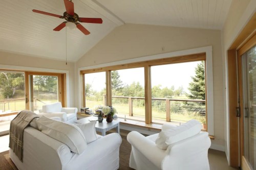 Bright, airy living room with white furniture, large windows, and a ceiling fan, overlooking a scenic outdoor view.