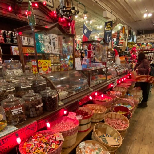 A colorful candy shop with jars and baskets filled with various candies, illuminated by festive lights.