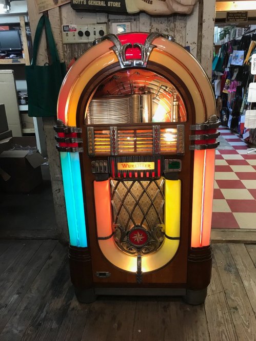 A vintage Wurlitzer jukebox with colorful lights, displayed in a rustic store setting.