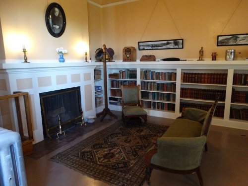 Cozy room with a fireplace, bookshelves filled with books, two chairs, and decorative items on the walls.