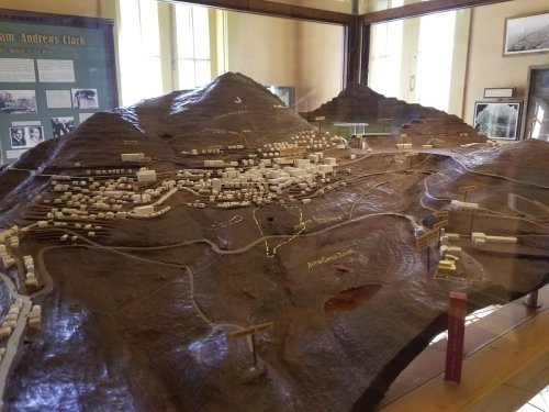A detailed topographical model of a mountainous area with buildings and roads, displayed in a glass case.
