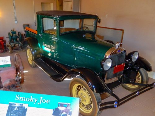 A vintage green truck named "Smoky Joe" displayed in a museum, with yellow wheels and a classic design.