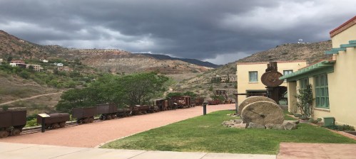 A scenic view of a historic mining site with old train cars, mountains, and a cloudy sky in the background.