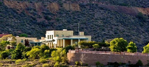 A large, modern building surrounded by greenery, set against a hilly landscape.