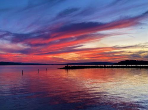 A vibrant sunset over a calm lake, with colorful clouds reflecting on the water's surface.
