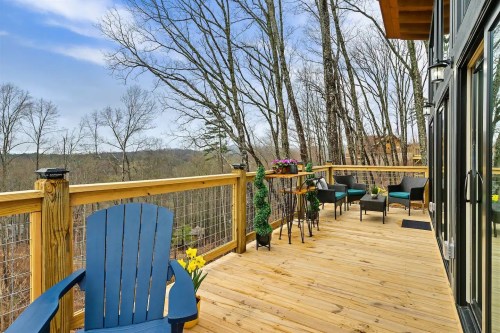 A wooden deck with blue chairs and potted plants, surrounded by trees and a scenic view in the background.
