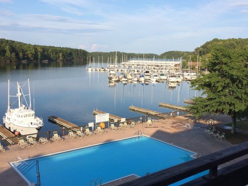 A serene lake view with a marina, boats docked, and a swimming pool in the foreground under a clear blue sky.