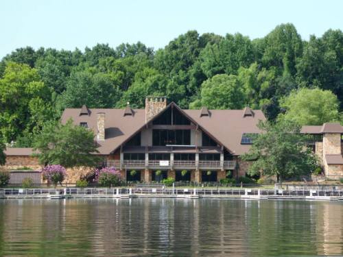 A large, rustic lodge with a stone facade, surrounded by greenery, reflected in a calm lake.