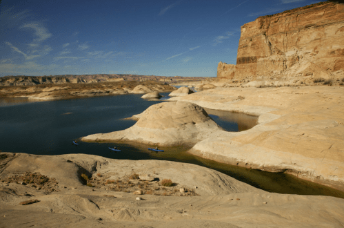 A serene desert landscape with a calm lake, rocky formations, and clear blue skies.