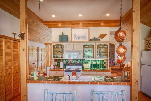 Bright kitchen with wooden accents, green tile backsplash, and a cozy dining area in the background.
