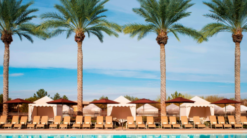A serene poolside scene with palm trees, lounge chairs, and umbrellas under a clear blue sky.