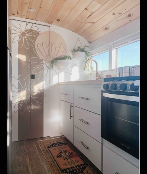A bright, modern kitchen with floral decor, white cabinets, and a stove, featuring natural light from large windows.