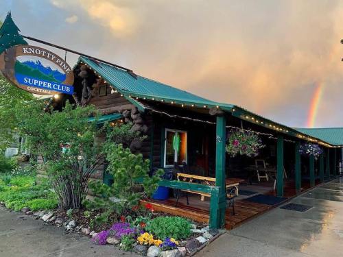 A charming log cabin restaurant with a green roof, surrounded by flowers and a rainbow in the background.