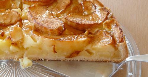 A slice of apple tart with golden-brown apple slices on a flaky crust, served on a glass plate.
