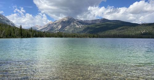 A serene lake surrounded by mountains and lush greenery under a partly cloudy sky.