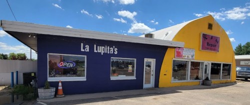 A colorful building with a purple side labeled "La Lupita's" and a yellow side for a repair shop, under a blue sky.