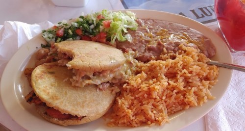 A plate of food featuring rice, refried beans, salad, and two stuffed tortillas with melted cheese and toppings.