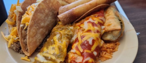 A plate of assorted Mexican food including tacos, enchiladas, and taquitos, served with rice.