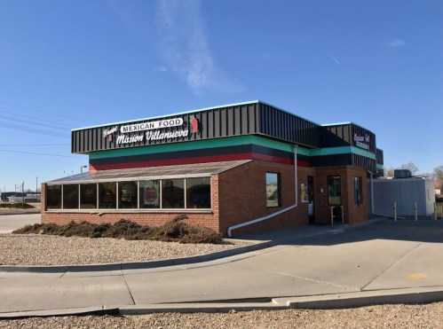 A colorful Mexican restaurant with large windows and a sign reading "Mexican Food Mission Volanera" against a clear blue sky.