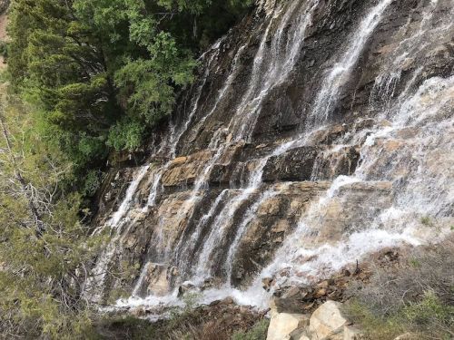 A cascading waterfall flows over rocky terrain, surrounded by lush green trees and vegetation.