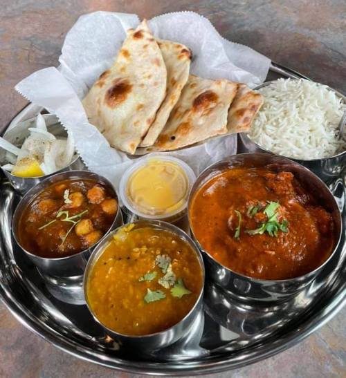 A stainless steel platter with naan, rice, and three bowls of colorful curries garnished with herbs.