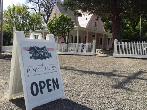 A sign reading "OPEN" in front of a charming pink house, which serves as a cheese and charcuterie shop.