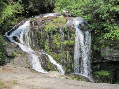 A serene waterfall cascading over rocky terrain, surrounded by lush green foliage and moss.