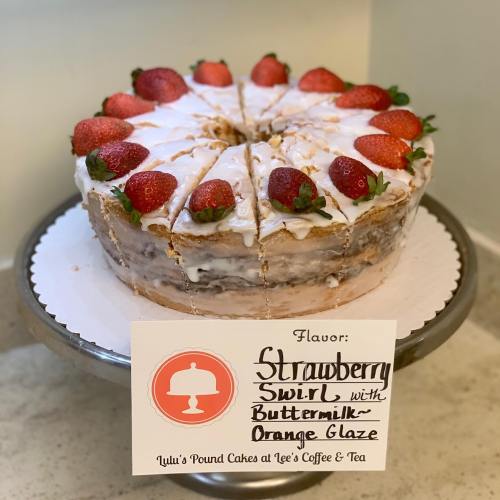 A layered strawberry cake topped with fresh strawberries and an orange glaze, displayed on a cake stand.