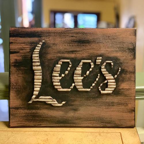 A wooden sign with the name "Lee's" carved in a decorative font against a rustic background.