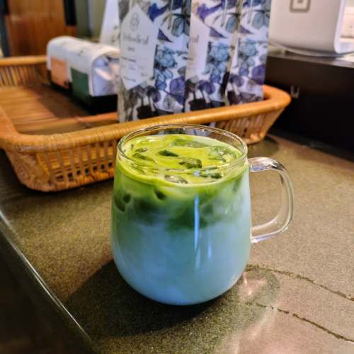A glass mug filled with layered iced matcha and milk, placed on a countertop with a woven basket in the background.