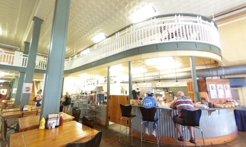 A cozy café interior with a curved balcony, wooden tables, and patrons seated at the bar enjoying their meals.