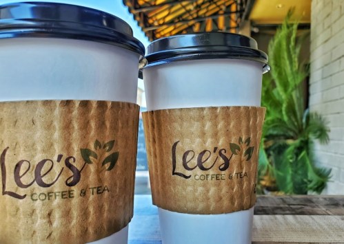 Two coffee cups with paper sleeves, featuring the logo "Lee's Coffee & Tea," set against a blurred background.