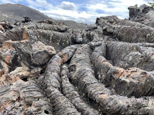 Close-up of textured, dark volcanic rock formations with a cloudy sky in the background.