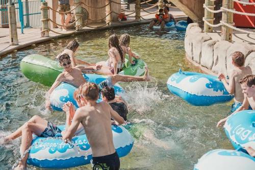 A group of children playing in a water park pool, splashing and riding colorful inner tubes.