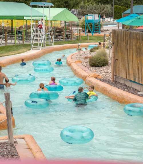 A lazy river at a water park with children floating on inner tubes and lifeguards overseeing the area.