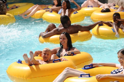 A group of people relax on yellow inner tubes in a pool, enjoying a sunny day. A woman and a child smile together.