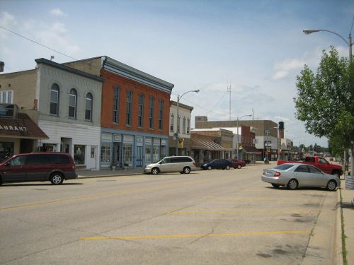 A quiet street lined with small shops and parked cars under a clear sky.