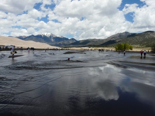A scenic landscape featuring a wet, reflective surface with mountains in the background and people enjoying the area.