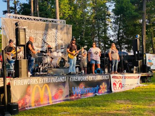 A live band performs on stage at an outdoor event, with banners for McDonald's and Walmart in the foreground.