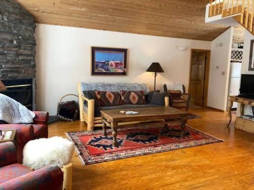 Cozy living room with wooden accents, a stone fireplace, patterned rugs, and comfortable seating.