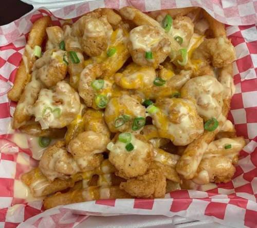 A box of loaded fries topped with cheese, shrimp, and green onions, served in a red and white checkered paper.