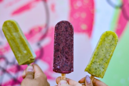 Three colorful popsicles on sticks held up against a vibrant, graffiti-style background.