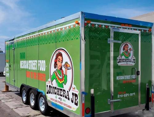 A green food trailer with "Lonchera JB" and "Mexican Street Food" signage, featuring a woman holding a taco.