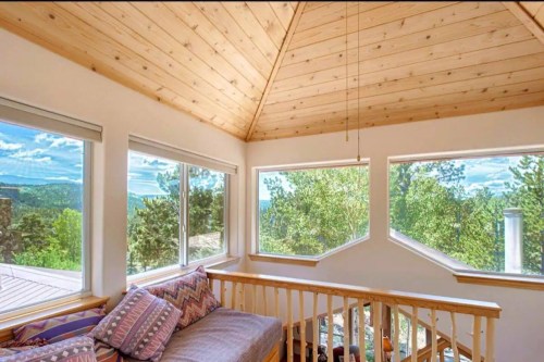 Cozy interior with a wooden ceiling, large windows showcasing a scenic view of trees and mountains.