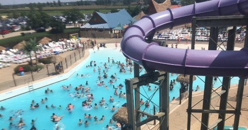 A water park scene with a purple slide, a crowded pool, and sunbathers enjoying a sunny day.