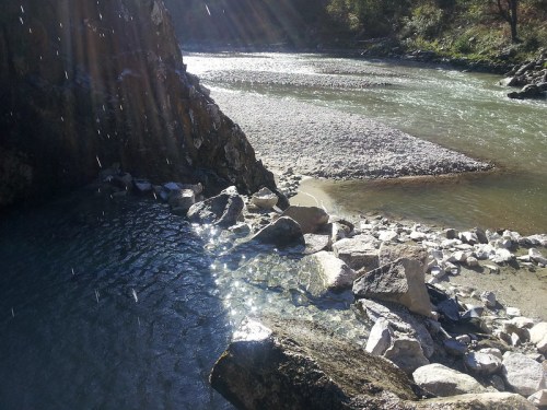 A serene river scene with sunlight streaming down, rocky banks, and clear water flowing gently.